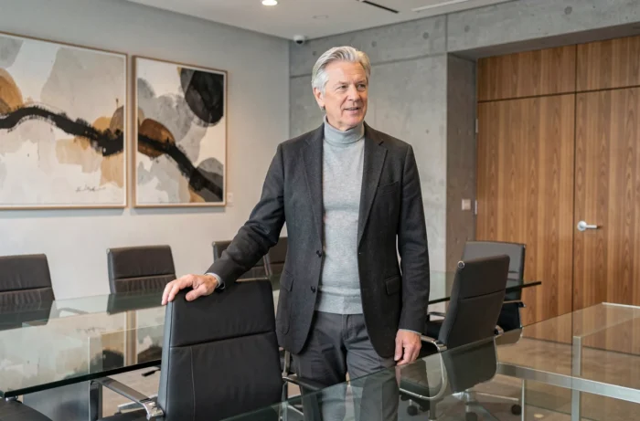 Homme d'affaires expérimenté s'adressant à une salle de conférence moderne, évoquant le leadership et la carrière d'un personnage influent